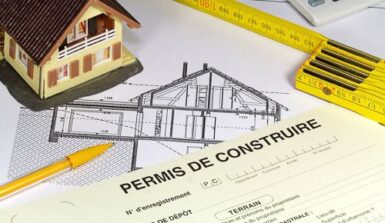 Dossier de permis de construire posé sur une table avec un mètre déroulant et une maison